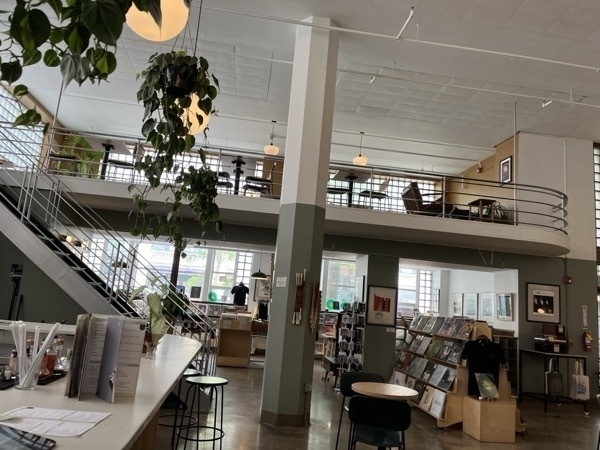 A photo from a coffee shop and record store, with hanging plants, mid-century railings, and a green/grey color palette