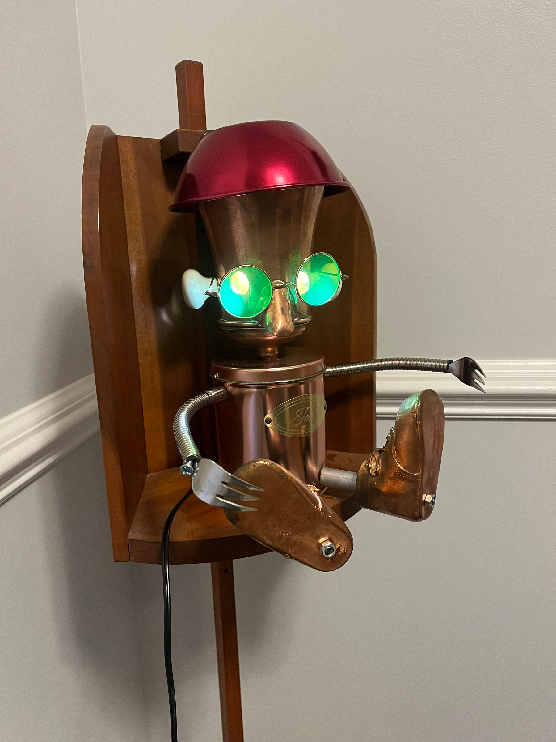 a lamp shaped like a robot, made of discarded parts welded together. The light comes from the eyes, wearing green glasses