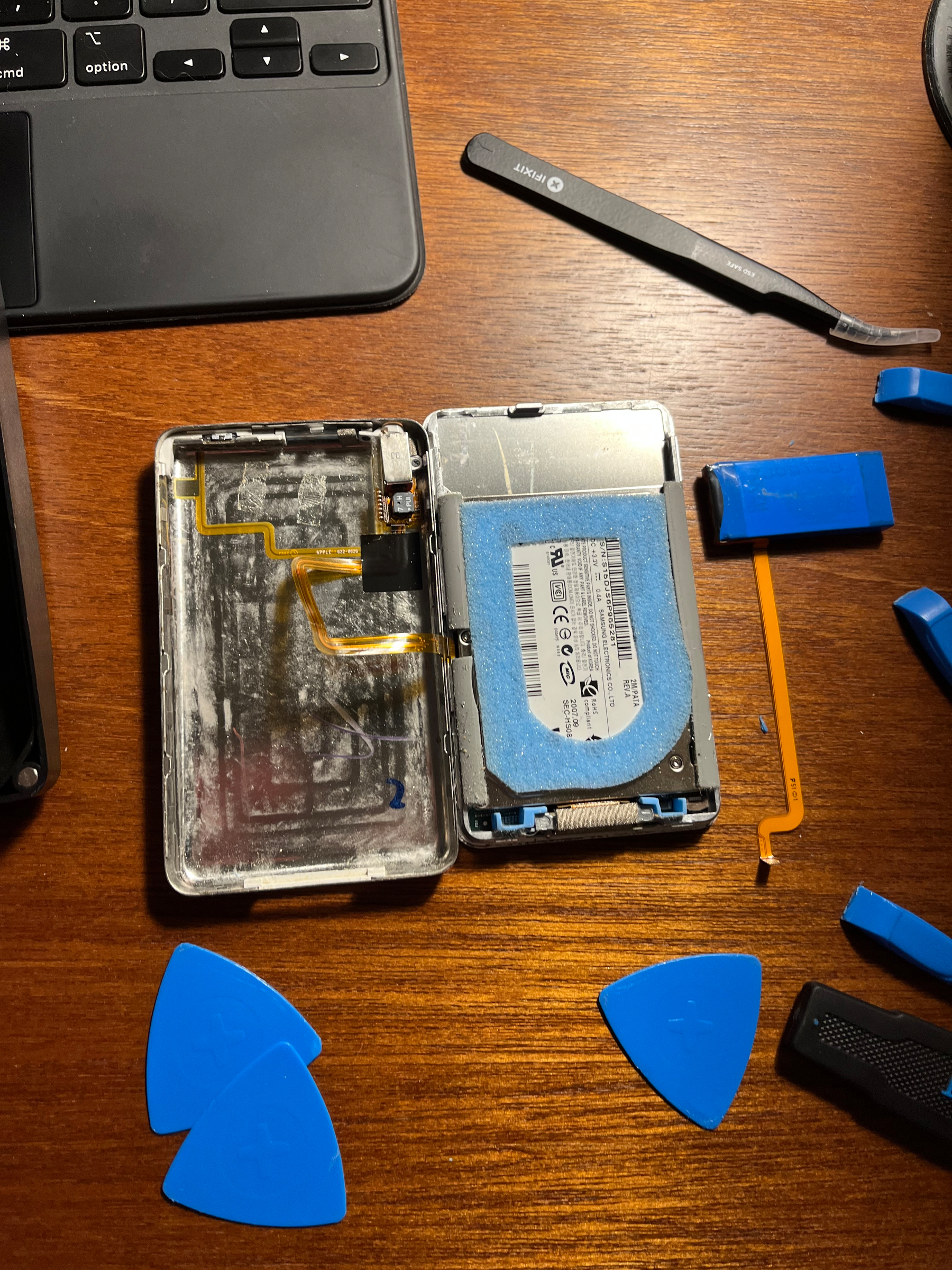 An iPod, opened up with its battery detached and pry tools everywhere 